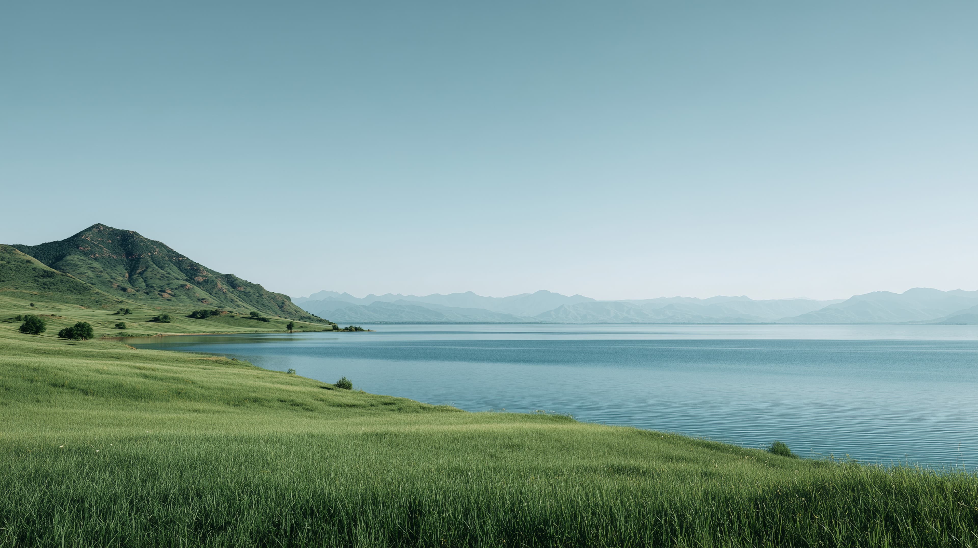 Tranquil grassy shoreline beside a calm blue lake under clear sky - High Resolution calm Wallpaper for Mobile and Desktop