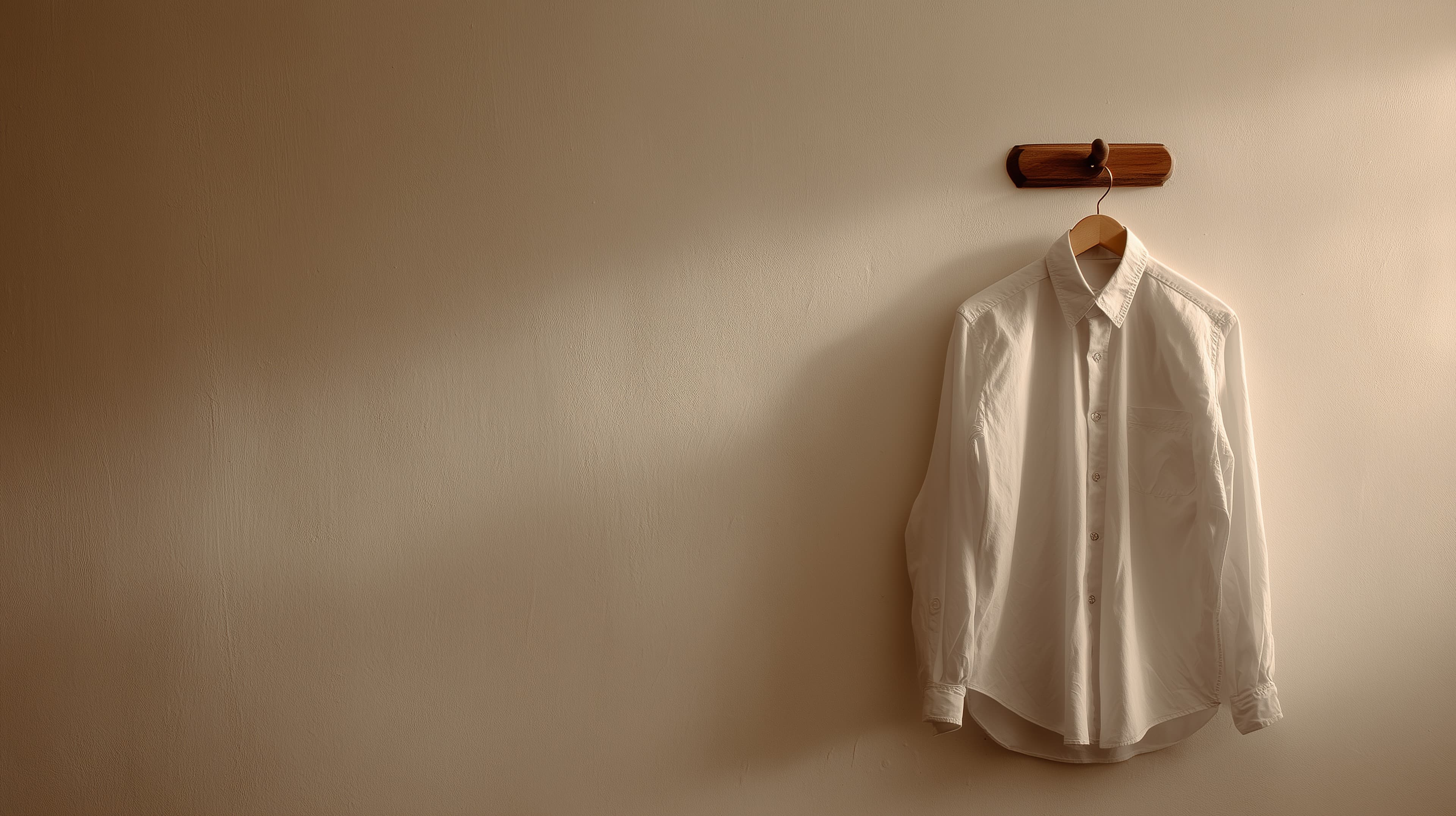 Minimalist White Shirt on Wooden Hanger Under Warm Wall Light - High Resolution minimalist Wallpaper for Mobile and Desktop